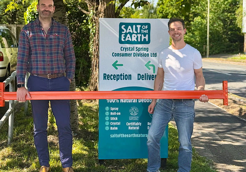 Thomas from Salt of the Earth and Brett Sanders from The Natural Deodorant Co. standing together outside the Salt of the Earth warehouse in Hampshire, holding orange warehouse racking equipment during their collaboration visit