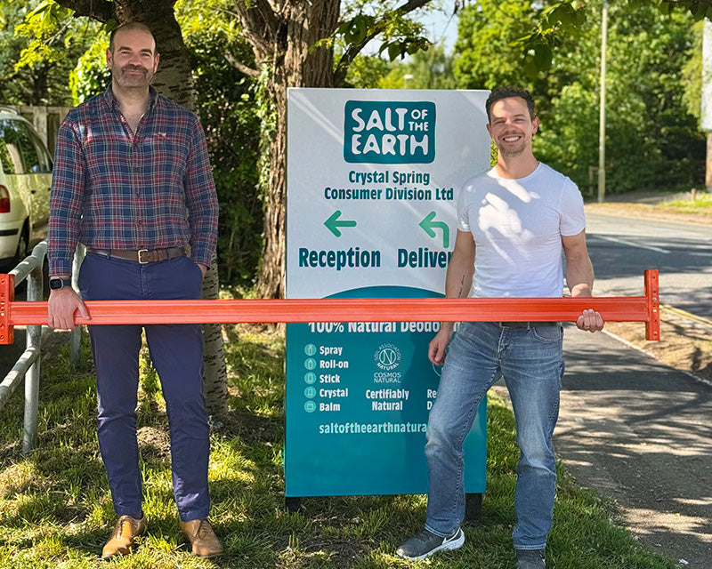 Thomas from Salt of the Earth and Brett Sanders from The Natural Deodorant Co. standing together outside the Salt of the Earth warehouse in Hampshire, holding orange warehouse racking equipment during their collaboration visit